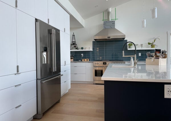 Kitchen with vaulted ceilings, white cabinetry and blue tile backsplash