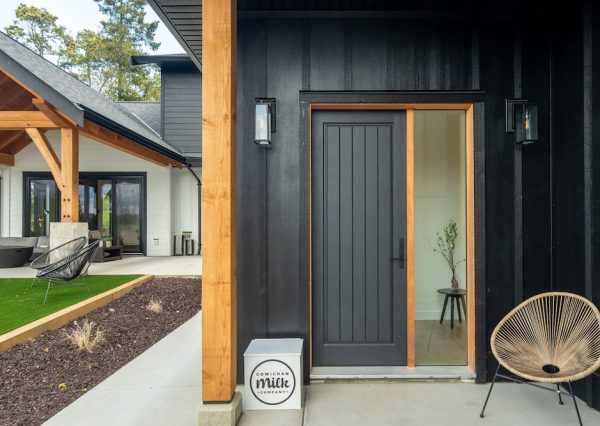 Black front door with black board and batten siding and wood beam
