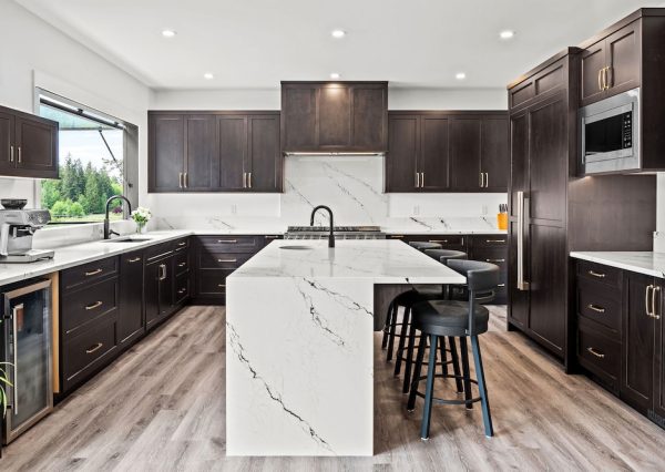 Black cabinetry in kitchen with gold hardware and cabinet front appliances and large pass through window
