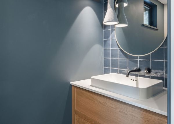 Sculptural pendant lights, round brass mirror and glossy dark tile create a dramatic powder room.