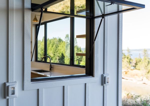 Black-framed awning window set into white board-and-batten siding beneath a warm wood soffit.