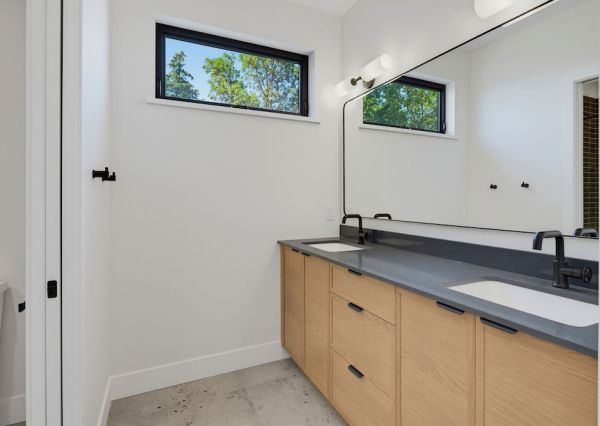 Natural wood double vanity with dark countertop, black fixtures and an oversized wall mirror.