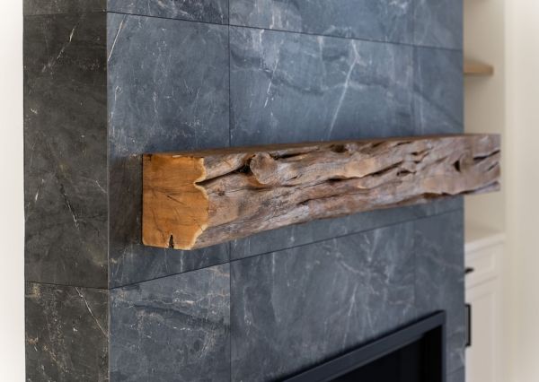 Rustic live-edge wood mantel against large-format dark stone fireplace tile in a modern waterfront home.
