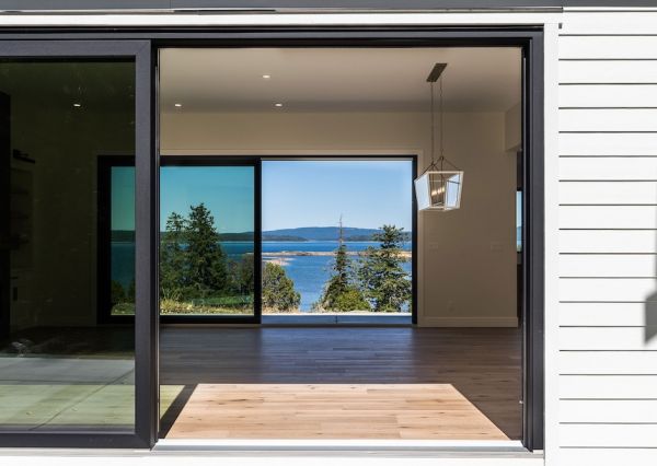 Large black-framed sliding glass doors frame an expansive ocean view from inside the waterfront home.