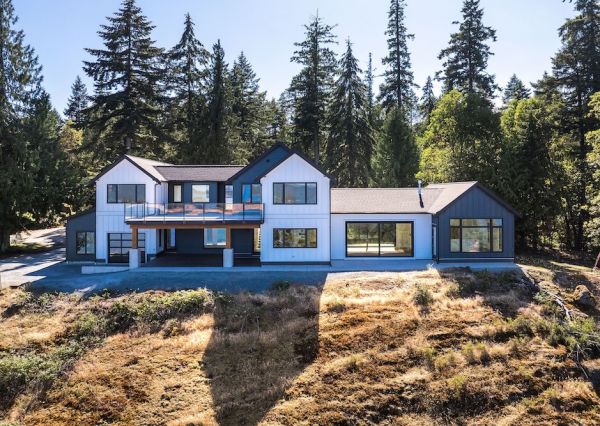 Modern waterfront custom home with contrasting white and dark siding, multiple gables and expansive windows.