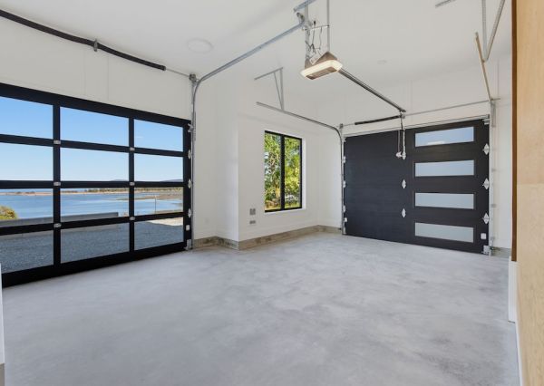 Finished garage with black glass-panel doors, polished concrete floor and views toward the waterfront.