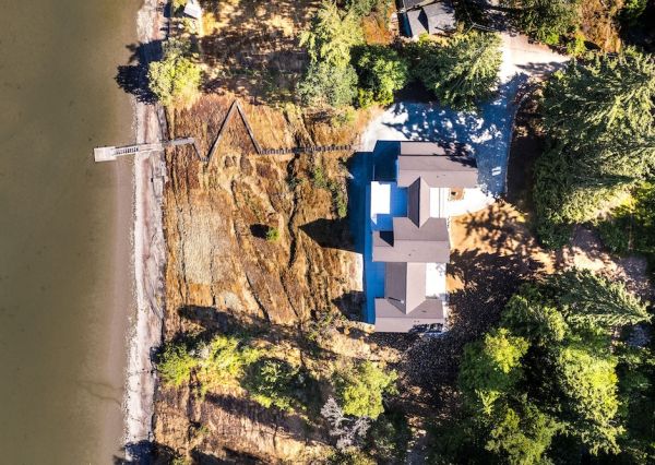 Aerial view of a waterfront property with a custom home, rocky shoreline, private dock and surrounding forest.